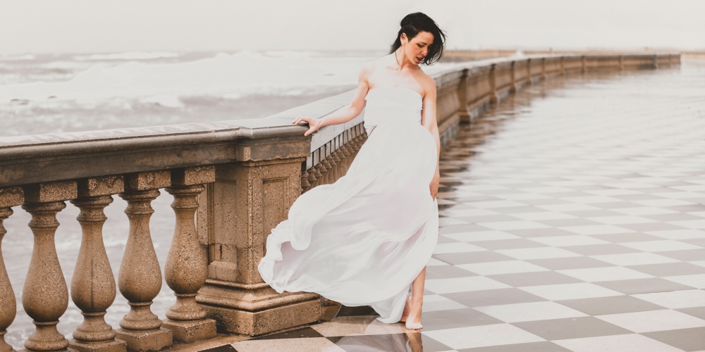 Shooting di moda al mare in piazza a Livorno vento e vestito bianco elegante cinematografica
