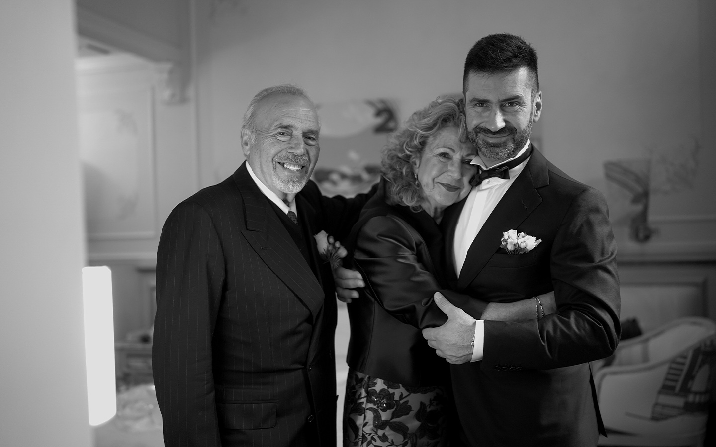 sposo mentre viene abbracciato da entrambi i genitori fotografia in bianco e nero piena di emozioni luxury wedding